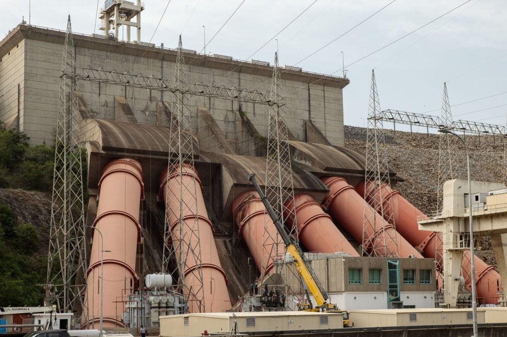 Usina hidrelétrica com grandes tubulações e linhas de transmissão de energia.