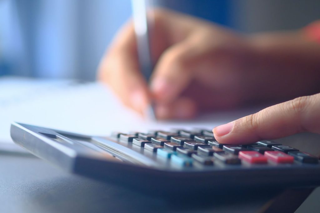 Mãos usando uma calculadora e fazendo anotações em uma planilha de orçamento.