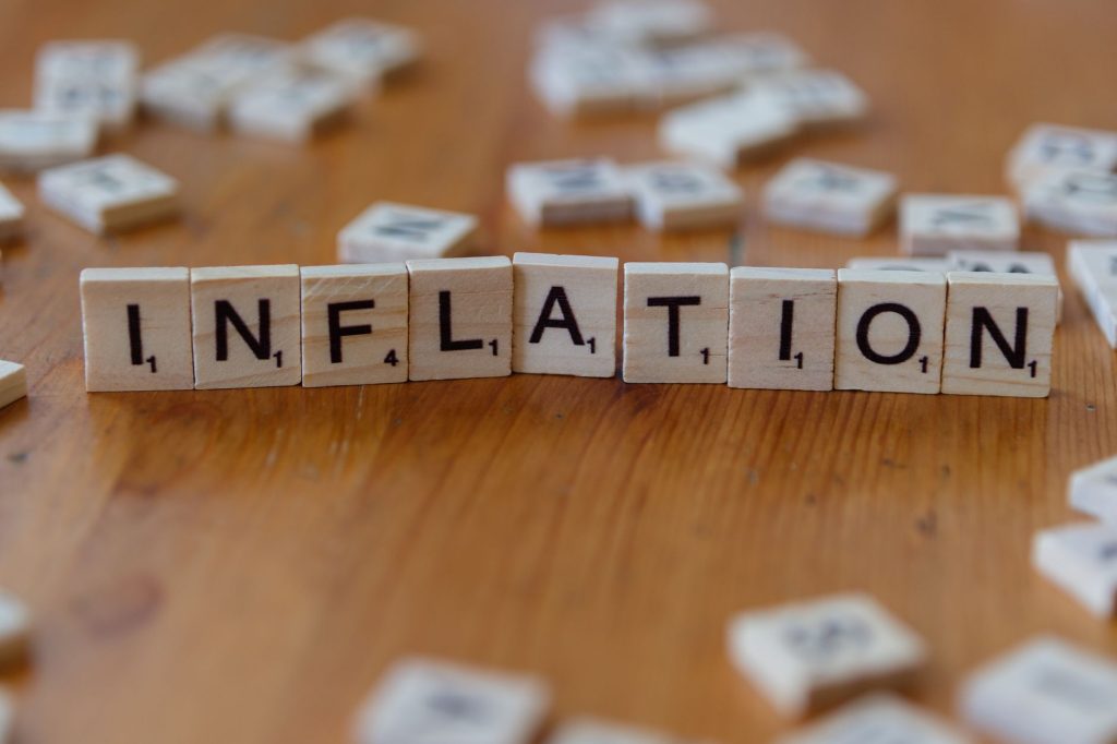 Peças de jogo de palavras formando a palavra “INFLATION” sobre uma mesa de madeira.